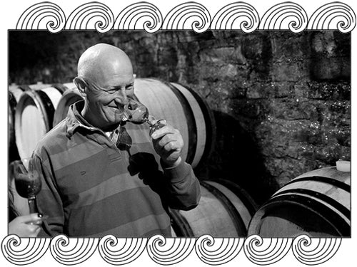 Claude Dugat tasting wine among barrels in his Gevrey-Chambertin cellar, framed with Dynamic Cellars wave design