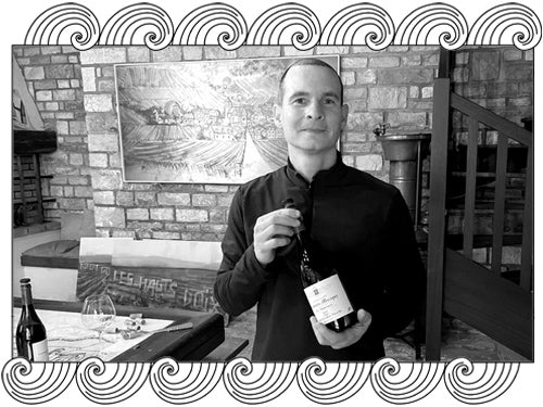 Domaine Groffier, Chambolle-Musigny winemaker, holding a bottle in his cellar, framed with Dynamic Cellars wave design