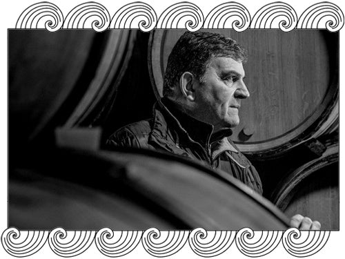 Emmanuel Rouget, Vosne-Romanée winemaker, among oak barrels in his cellar, framed with Dynamic Cellars wave design