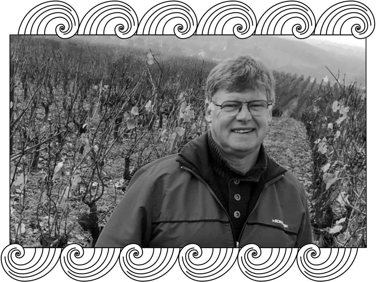 Leroy Richard in his vineyard among bare winter vines on a slope, framed with Dynamic Cellars wave design