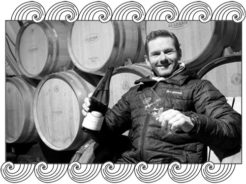 Stephane Aladame, Burgundy winemaker, in his barrel cellar with a bottle, framed with Dynamic Cellars wave design